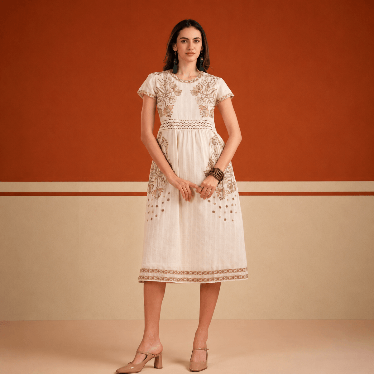 Woman wearing a white lace dress against an orange and beige wall.