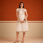 Woman wearing a white lace dress against an orange and beige wall.