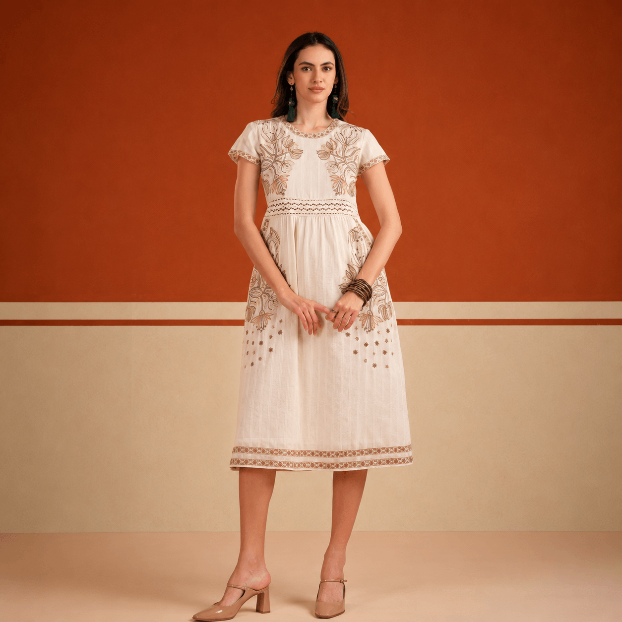 Woman wearing a white lace dress against an orange and beige wall.